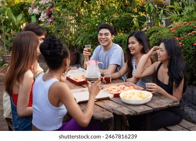 Six young friends hanging out, laughing and having a nice picnic outdoors by the backyard enjoying pizza and drinks - Powered by Shutterstock