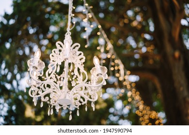 Six-light Crystal Chandelier And Garland Hanging From The Tree. Decorating A Wedding Dinner Outside.