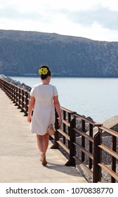 Sixties Retro Style: Rear View Of A Woman With A Beehive Hairdo, Devorated With Artifical Flowers, Walking On A Harbour Pier Footbridge