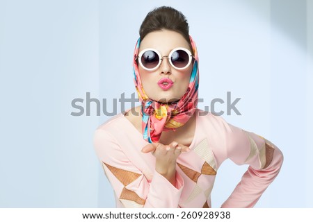 Sixties style girl blowing a kiss. Retro fashion with silk scarf and sunglasses.