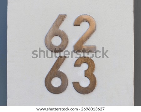 Sixty two and sixty three, or 62 and 63, metal house numbers in the street. Arabic numerals: six, two and six, three. Traditional digits in the white plastered wall background, close up.