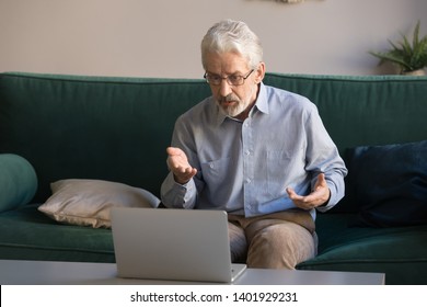 Sixty Years Old Man Sit On Sofa In Living Room Makes Videocall Looking At Computer Screen Use App Teleconference, Grandfather Having Problems With Electronic Device Feels Annoyed Embarrassed Concept