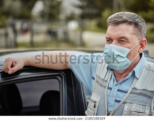 Sixty-year-old man in\
a medical mask near the\
car