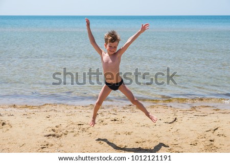 Six-year-old boy in black speedo jumping into the sea and smiles.