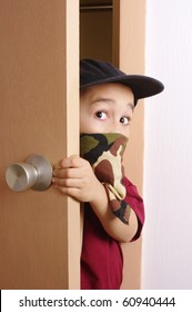 Six-year-old Boy Wearing A Camouflage-colored Bandanna Mask, Sneaking In Through A Door