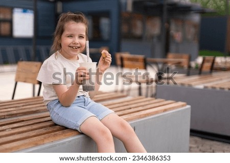 A six-year-old girl drinks a milkshake and eats a kidney. Sweets in children's lives, street food. High quality photo