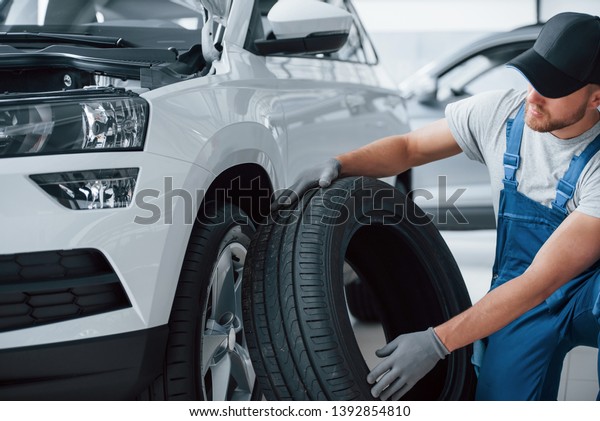 Size comparison.\
Mechanic holding a tire at the repair garage. Replacement of winter\
and summer tires.