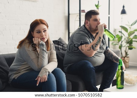 size plus boyfriend drinking beer and girlfriend looking away at home