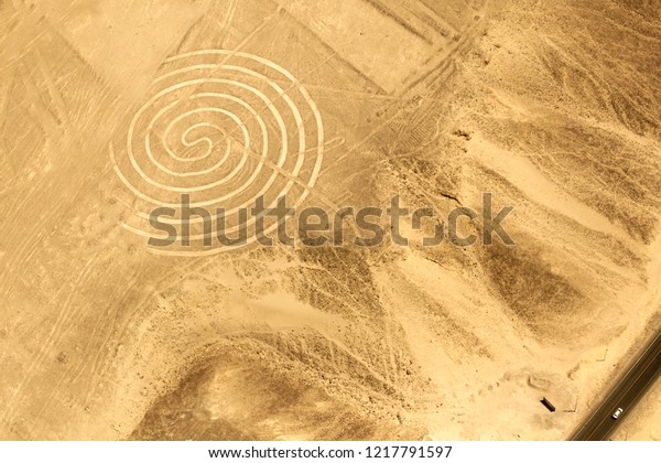 The size and scale of a spiral pattern on the\
floor of the Nazca desert is emphasised by the miniscule car\
driving past on the nearby\
highway