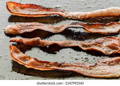 Sizzling bacon frying on a griddle pan.