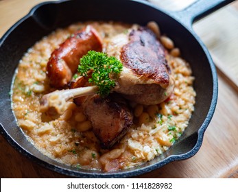 Sizzling hot, rich, slow-cooked Trio Cassoulet of duck confit, pork belly and smoked sausage on a bed of white beans in a black cast iron pan on a wooden table. Natural Light. - Powered by Shutterstock