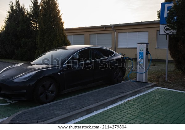 Skarbimierz Osiedle,\
Poland - January 9, 2022. A static shot of a solid black Tesla\
Model 3 dual motor charging at the EV+ AC charging station in a\
sunny winter day. Selective\
focus.