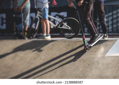 Skate Park View With Kids On A Kick Scooter Doing Tricks And Stunts, Boys In A Skate Park Riding Bmx Bike And Skate, Playing And Enjoying Summer On New Ramp, Teenagers Skateboarders And Bmx Riders 