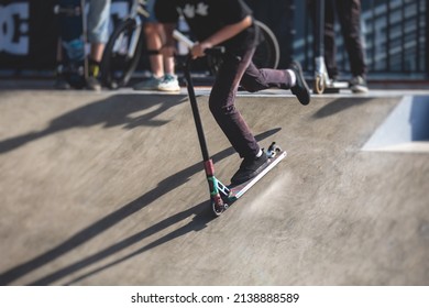 Skate Park View With Kids On A Kick Scooter Doing Tricks And Stunts, Boys In A Skate Park Riding Bmx Bike And Skate, Playing And Enjoying Summer On New Ramp, Teenagers Skateboarders And Bmx Riders 