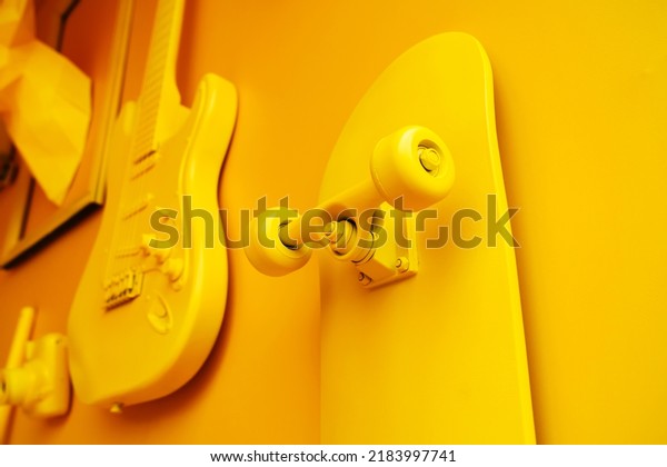 A\
skateboard and an electric guitar painted with yellow paint hang\
against the background of the wall. Restoration of old items and\
use in interior decoration. Selective focus.\
Foreground
