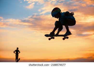 Skateboarder in action. Black silhouette of young boy making air trick with grab on skate in skatepark on sky with sun background. Street culture, skateboard riding lessons. Weekend activities.