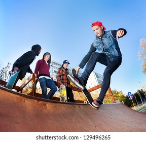 Skateboarder With Friends In Skatepark Jumping In The Halfpipe