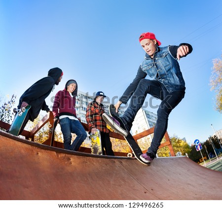 Skateboarder with friends in skatepark jumping in the halfpipe
