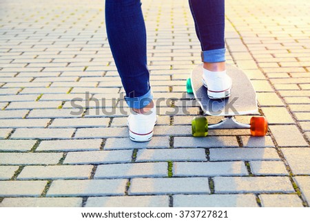 Skateboarder girl legs and board close up. Blue jeans and white sneakers. Extreme sport. Youth lifestyle. Street, pavement.