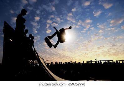 Skateboarder jumping on a ramp at sunset with large audience in background. - Powered by Shutterstock