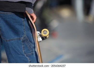 Skater Holding Old Scratches Skateboard Deck In Hand In Outdoor Skatepark