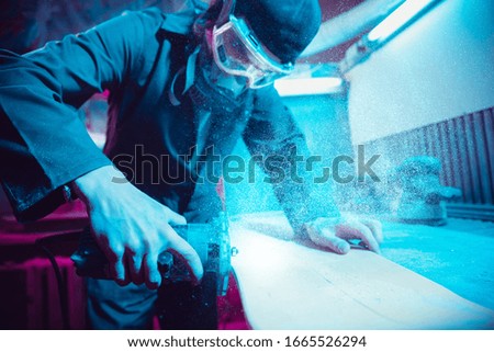 Skater in process of making his own skateboard, longboard - open business concept. Neon lighted studio of creating skateboards. Concept of openspace, craft production, workshop. Polishes, paints.