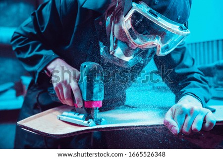 Skater in process of making his own skateboard, longboard - open business concept. Neon lighted studio of creating skateboards. Concept of openspace, craft production, workshop. Polishes, paints.