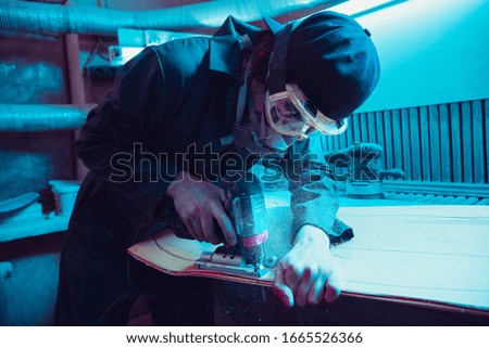 Skater in process of making his own skateboard, longboard - open business concept. Neon lighted studio of creating skateboards. Concept of openspace, craft production, workshop. Polishes, paints.