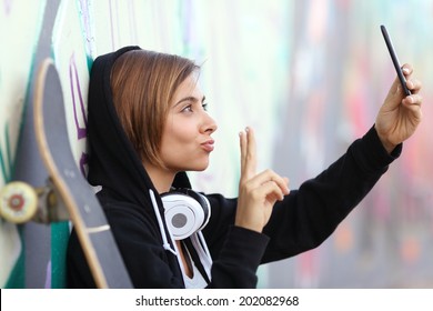 Skater teenager girl taking a photograph with smart phone camera with blurred graffiti wall in the background           