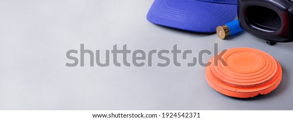Skeet\
shooting. Clay target, noise cancelling headphones, bullet shell,\
and blue cap on gray. Wide banner with copy\
space