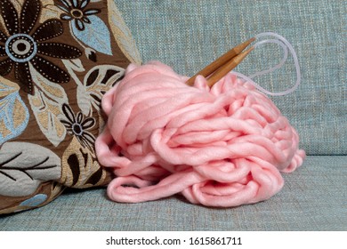 Skein Of Giant Merino Pink Yarn For Arm Knitting With Large Knitting Needles On A Blue Sofa