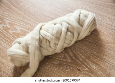 A skein of large-knit beige merino wool threads on a wooden floor.