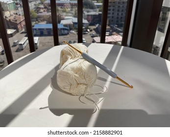 A Skein Of White Cotton Yarn And A Crochet Hook On A White Table