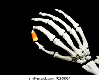 Skeleton Hand Holding A Piece Of Candy Corn Isolated On A Black Background