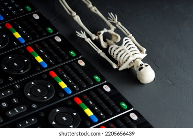 The Skeleton Of A Person Lies Diagonally Down, Parallel To It Are Remote Controls From The TV. Death And Life Of A Person Are Accompanied By Television