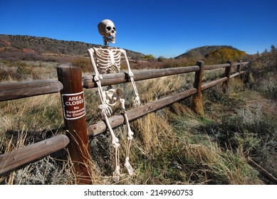 Skeleton resting on wooden pole rail fence in area closed to hikers next to no trespassers no climbing sign