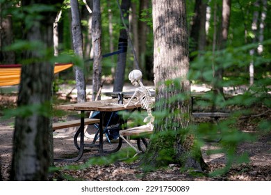 A skeleton spending some time in a campground sitting at a picnic table.