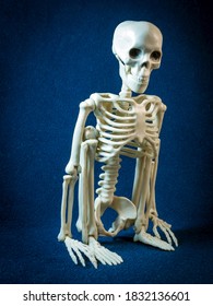 A Skeleton Is Squatting On A Dark Background.