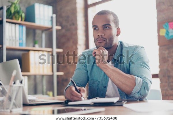 Skeptic,\
unsure, uncertain, doubts concept. Young african student is making\
decision sitting at the office in casual\
smart
