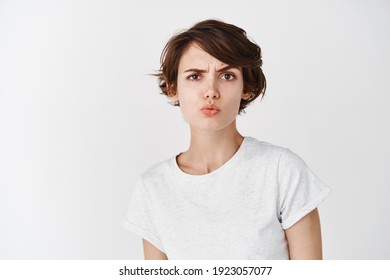 Skeptical caucasian woman look perplexed at camera, pucker lips and raising eyebrow suspicious, feeling doubtful or unsure, standing on white background.