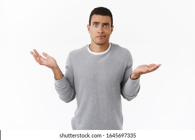 Skeptical and confused, disappointed hispanic guy dont understand anything, shrugging, spread hands sideways, smirk annoyed and frustrated, standing indecisive over white background