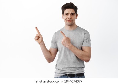 Skeptical Handsome Guy Points Aside And Smirk With Disbelief, Have Doubts, Being Unsure, Standing Over White Background