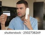 Skeptical looking man holding credit card during phone call 