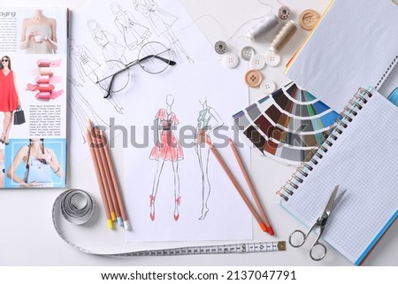 Sketches of clothes and different stuff on white table, flat lay. Fashion designer's workplace