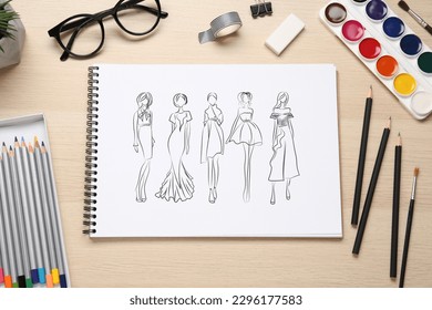 Sketches of different clothes in pad on wooden table. Fashion designer's desk with stationery, flat lay - Powered by Shutterstock