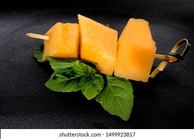 A Skewer Of Cantaloupe Melon Isolated On A Black Plate