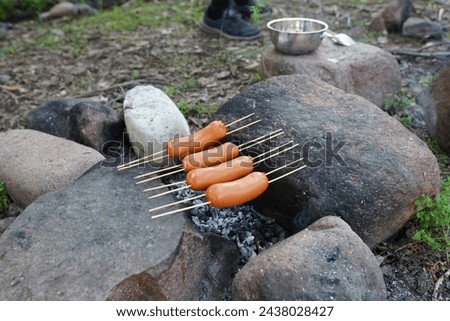 Skewered sausages heat up on hot stones, using an inventive method of cooking without a flame, showcasing camping ingenuity.