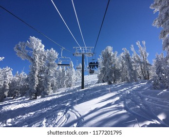 Ski Chair Lift Ascends Over Deep Snow And Snow Covered Trees. Sunny Blue Skies Overhead.