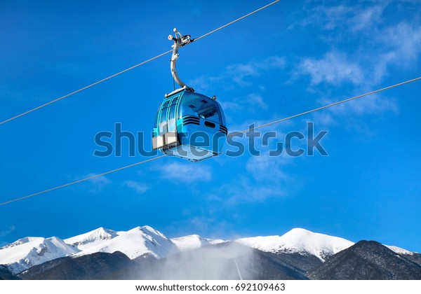 Ski lift, cable car cabin in\
bulgarian ski resort and snow mountain peaks at the\
background