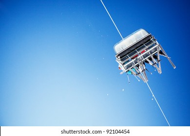 Ski Lift Carrying Unrecognizable Skiers Up To The Clear Blue Sky